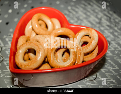 Glasierte Bagels auf rotem Teller in Herzform auf grauem Hintergrund mit geknallten Wörtern. Stockfoto