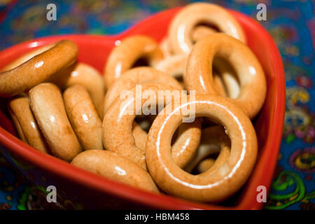 Close-up verglaste Bagels auf rotem Teller in Form von Herzen auf farbigem Hintergrund. Stockfoto