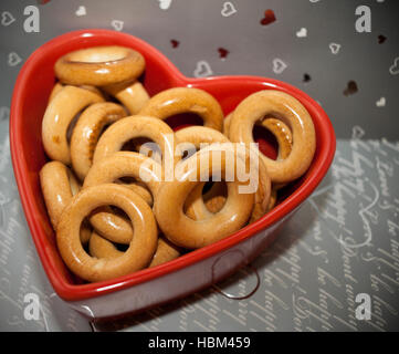 Bagels auf rotem Teller in Herzform auf grauem Hintergrund. Stockfoto