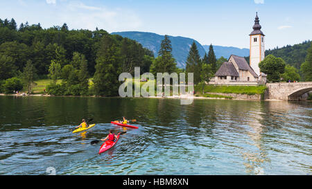 Triglav Nationalpark, Oberkrain, Slowenien.  Kinder Kajak auf See von Bohinj.  Die Kirche ist St. Johannis (Cerkev Sv Janeza) an das Dorf Rippe Stockfoto