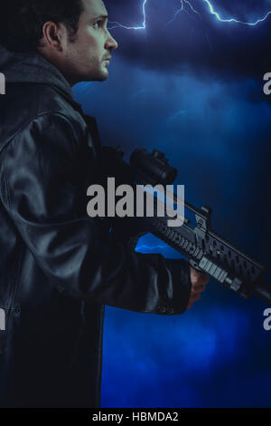 Mann mit Leder Jacke und Angriff Gewehr über Sturm Hintergrund Stockfoto