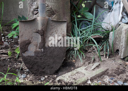 Eine schmutzige Schaufel schlammbedeckt gegen einen Baum Stockfoto