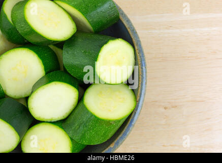 Enge Draufsicht auf eine alte Steingut-Schüssel gefüllt italienische Squash in Stücke auf einer hölzernen Tischplatte geschnitten. Stockfoto