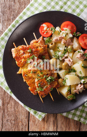 Spanische Kebab Pinchos Morunos und Salat Patatas Alinadas Nahaufnahme auf einer Platte. vertikale Ansicht von oben Stockfoto