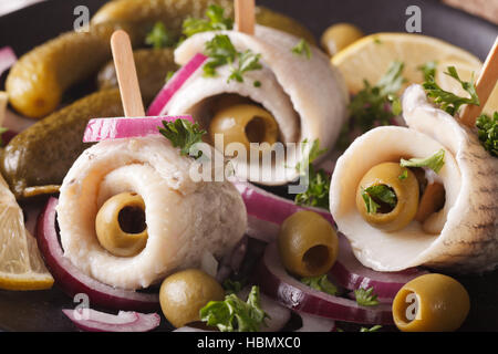 Rollmops Hering mit Oliven, Zwiebeln und Gurken Makro auf einem Teller. horizontale Stockfoto