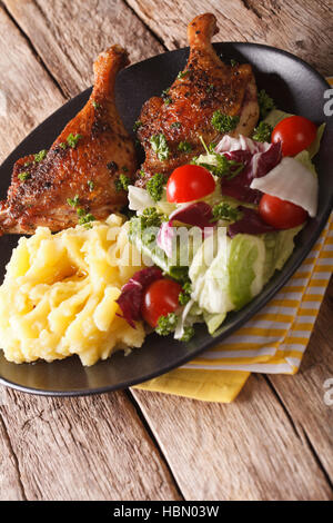 Gebratene Entenkeule mit gestampften Kartoffeln Beilagen und frischem Salat auf der Platte Nahaufnahme. vertikale Stockfoto