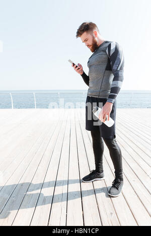 Läufer mit Wasser und Telefon. Mann steht zur Seite. Blick auf Telefon Stockfoto