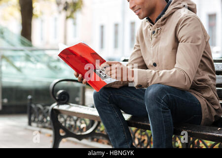 Foto von konzentrierten afrikanischen Jüngling hält Buch in Händen und lesen über Straße Hintergrund abgeschnitten. Stockfoto