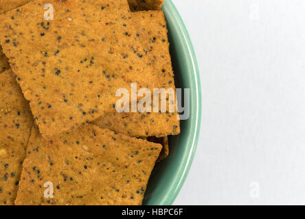 Enge Draufsicht des Gourmet-Teff Vollkorn Snack-Cracker in einer grünen Schale auf einer weißen Tischdecke. Stockfoto