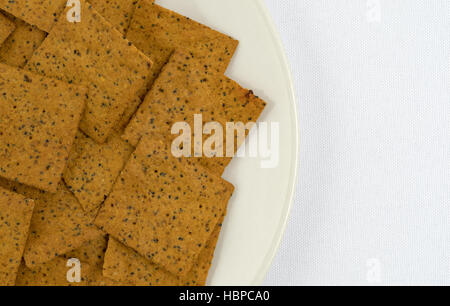 Enge Draufsicht des Gourmet-Teff Vollkorn Snack-Cracker auf einer Platte auf eine weiße Tischdecke. Stockfoto