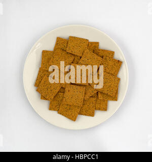 Draufsicht der Gourmet-Teff Vollkorn snack Cracker auf einer Platte auf eine weiße Tischdecke. Stockfoto