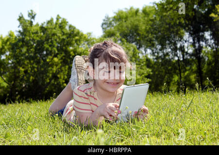 kleines Mädchen auf dem Rasen liegen und spielen mit TabletPC Stockfoto