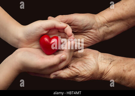 kleine Mädchen und ältere Frau rotes Herz in ihre Handflächen zusammen, Symbol der Liebe und Sorgfalt zu halten Stockfoto