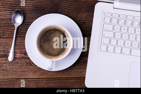 Weiße Tasse mit Löffel und Notebook auf natürliche Holztisch. Stockfoto