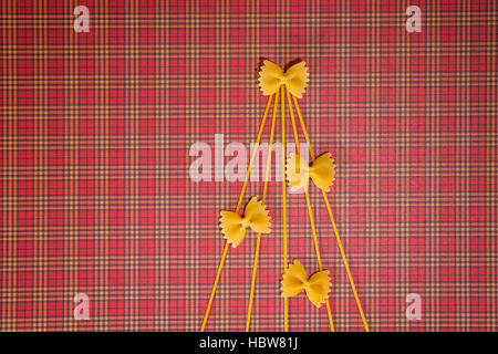 Weihnachtsbaum-Silhouette hergestellt aus Spaghetti und Farfalle auf rotem Quadrat. Flach zu legen. Ansicht von oben. Winter Urlaub Konzept Stockfoto