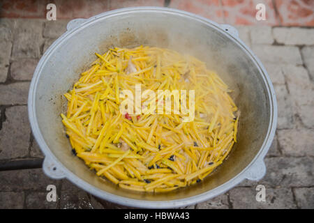 Pilaw in einem Metall große Kessel mit Knoblauch und gelben Karotten. Essen-Hintergrund. Stockfoto