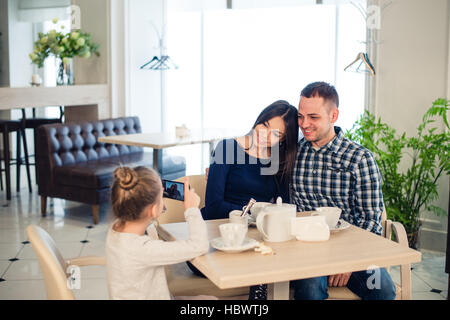 Familie, Elternschaft, Menschen Technologiekonzept - Nahaufnahme von glückliche Mutter, Vater und kleine Mädchen essen, Kind nehmen Foto per Smartphone im Restaurant Stockfoto