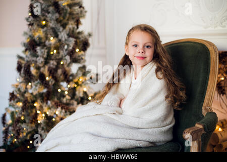 Niedliche kleine Mädchen sitzt durch den Weihnachtsbaum, eingehüllt in eine warme Decke zu Hause Stockfoto