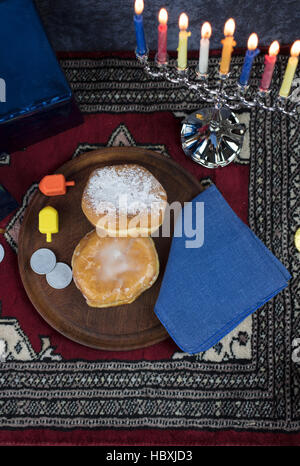 Hanukkah Menorah mit brennenden Kerzen, Geschenke, Dreidel und Gelee gefüllt Gebäck serviert auf einer Holzplatte für den Urlaub Stockfoto