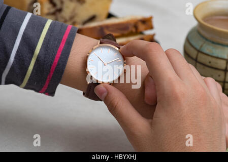 Klassische Armbanduhr auf des Mädchens Hand vor der heißen Schokolade und Kuchen Stockfoto