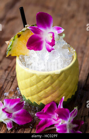 Tiki cocktail in einer Ananas-Becher mit frischer Ananas und Orchidee Blume Beilagen serviert. Stockfoto