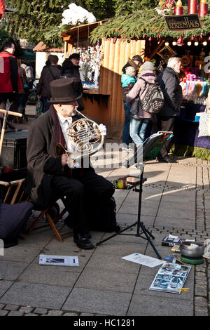 Weihnachten Handwerk Markt in Ludwigsburg, Deutschland, Shopper an Handwerker Ständen, während ein Top hüten Musiker ein Horn spielt. Stockfoto