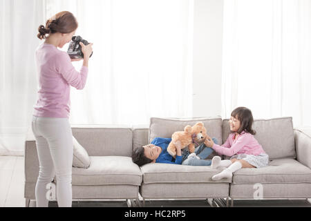 Liebevolle Mutter, die Aufnahme von ihrem Sohn und Tochter spielen mit Teddy-Bär auf dem sofa Stockfoto
