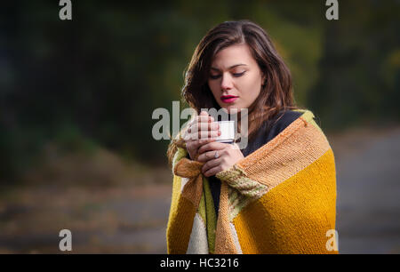 Trauriges Mädchen im Freien mit einer Tasse Kaffee (Tee) und in eine warme Decke gehüllt. Stockfoto