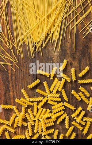 Vereinzelte italienische Pasta, gelb Fusilli und Spaghetti als Draufsicht Stillleben, Hintergrundbild auf rustikalem Holzbrett Stockfoto