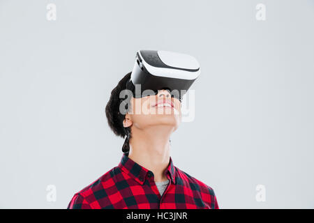 Bild von fröhlichen jungen asiatischen Mann gekleidet in lässigen Shirt in einem Käfig und virtual-Reality-Gerät tragen. Isoliert auf weißem Hintergrund. Stockfoto