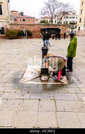 Eine alte Frau trinken aus einem Brunnen auf der Straße in Campo del Ghetto, Venedig, Italien Stockfoto