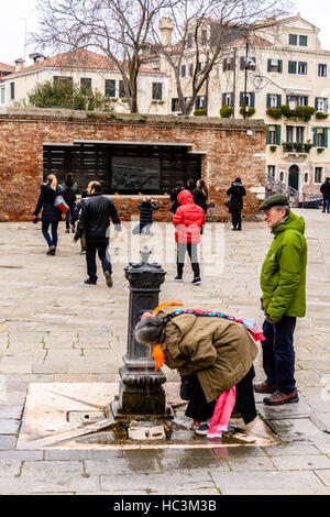 Eine alte Frau trinken aus einem Brunnen auf der Straße in Campo del Ghetto, Venedig, Italien Stockfoto