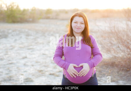 Junge schöne schwangere Frau auf einen Hintergrund Sonnenuntergang. 9. Monat der Schwangerschaft. Stockfoto