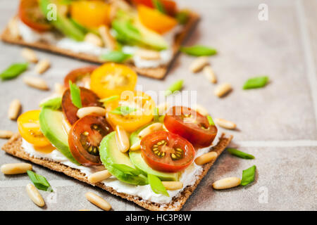 Gesund Roggen Knäckebrot Toast mit Frischkäse, frische Avocado, Cherry Tomaten und Pinienkernen Stockfoto