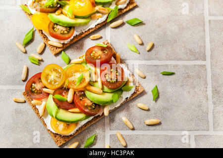 Gesund Roggen Knäckebrot Toast mit Frischkäse, frische Avocado, Cherry Tomaten und Pinienkernen Stockfoto