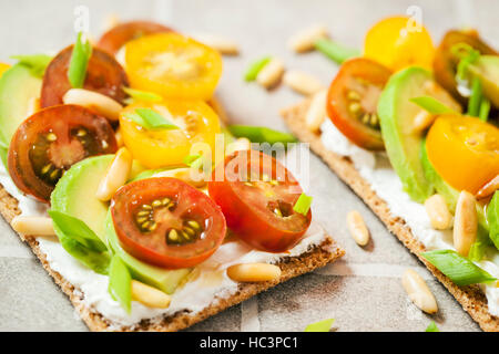 Gesund Roggen Knäckebrot Toast mit Frischkäse, frische Avocado, Cherry Tomaten und Pinienkernen Stockfoto