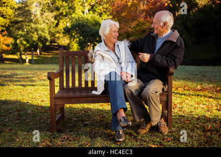 Älteres Ehepaar sitzen auf Bank lächelnd an einander im park Stockfoto