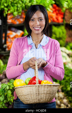 Lächelnde Frau halten Obst und Gemüse im Korb Stockfoto