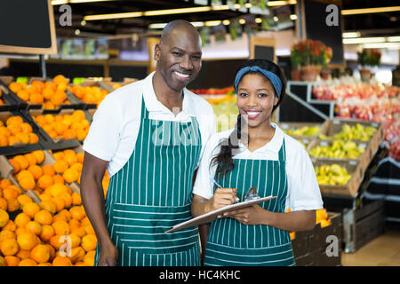 Lächelnde Personal schreiben in Zwischenablage im organischen Bereich des Supermarktes Stockfoto