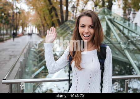 Lächelnde schöne junge Frau winken und sagen Sie Hallo im park Stockfoto