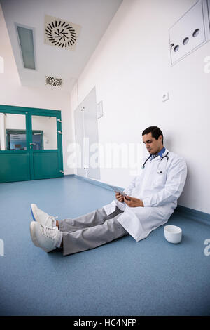 Arzt auf Boden sitzend und mit digital-Tablette in Gang Stockfoto