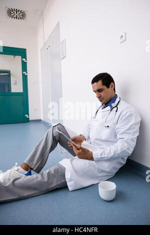 Arzt auf Boden sitzend und mit digital-Tablette in Gang Stockfoto