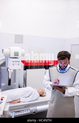 Arzt mit digital-Tablette und Patienten liegen auf X-Ray Maschine Stockfoto