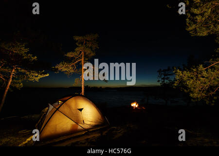 Lagerfeuer und Zelt in der Wildnis am See in der Nacht Stockfoto