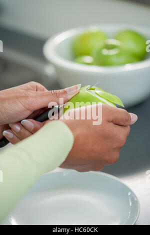 Weibliche Hände peeling Haut aus grünem Apfel mit einem Schälmesser Stockfoto