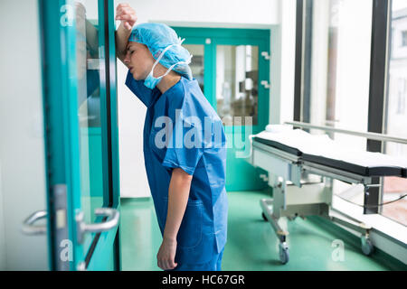 Traurige Chirurgen lehnte sich gegen die Glastür Stockfoto