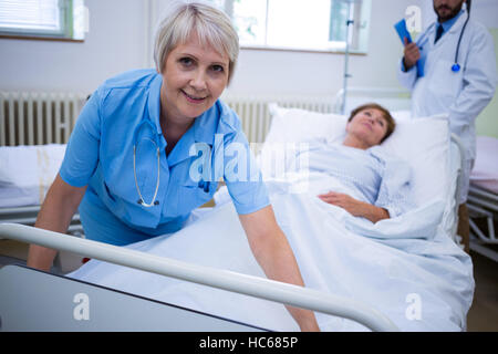 Lächelnde Krankenschwester erstreckt sich eine Decke über Patienten Stockfoto