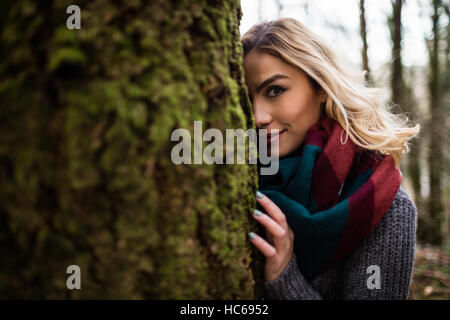 Schöne Frau versteckt sich hinter Baumstamm im Wald Stockfoto