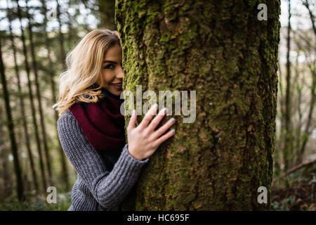 Schöne Frau versteckt sich hinter Baumstamm im Wald Stockfoto