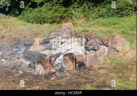 Burn out glimmenden Lagerfeuer Asche mit geschwärzter Protokolle in einem steinernen Feuerstelle. Die Glut noch glühende Stockfoto